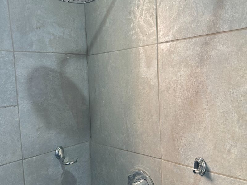 A modern shower enclosure featuring large format grey ceramic wall tiles, a chrome rainfall shower head, and a single-lever mixer tap.