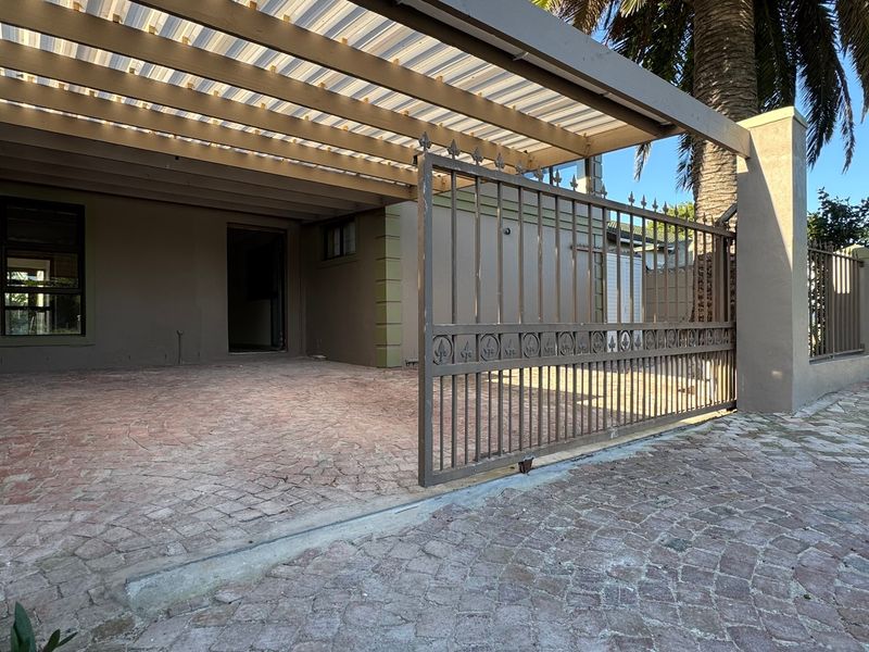 Front exterior view featuring a paved driveway, metal security gate, and a covered carport area.