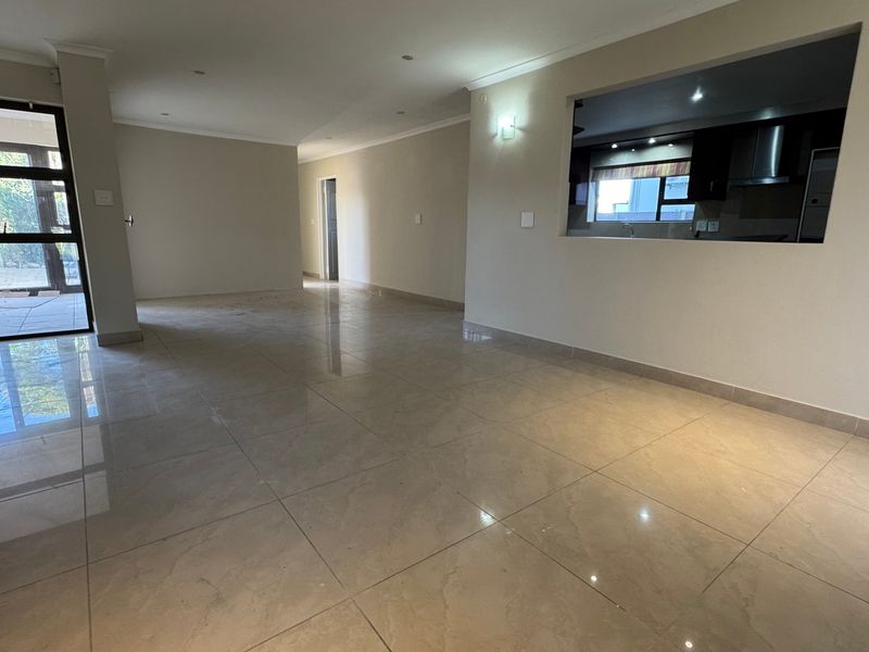 Spacious open-plan living area featuring polished porcelain floor tiles, recessed lighting, and a convenient serving hatch connecting to the kitchen.