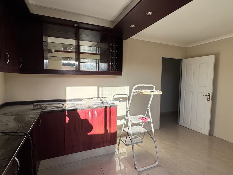 A functional kitchen area featuring dark wood-toned cabinetry, granite-look countertops, and neutral tiled flooring, currently in a vacant state.