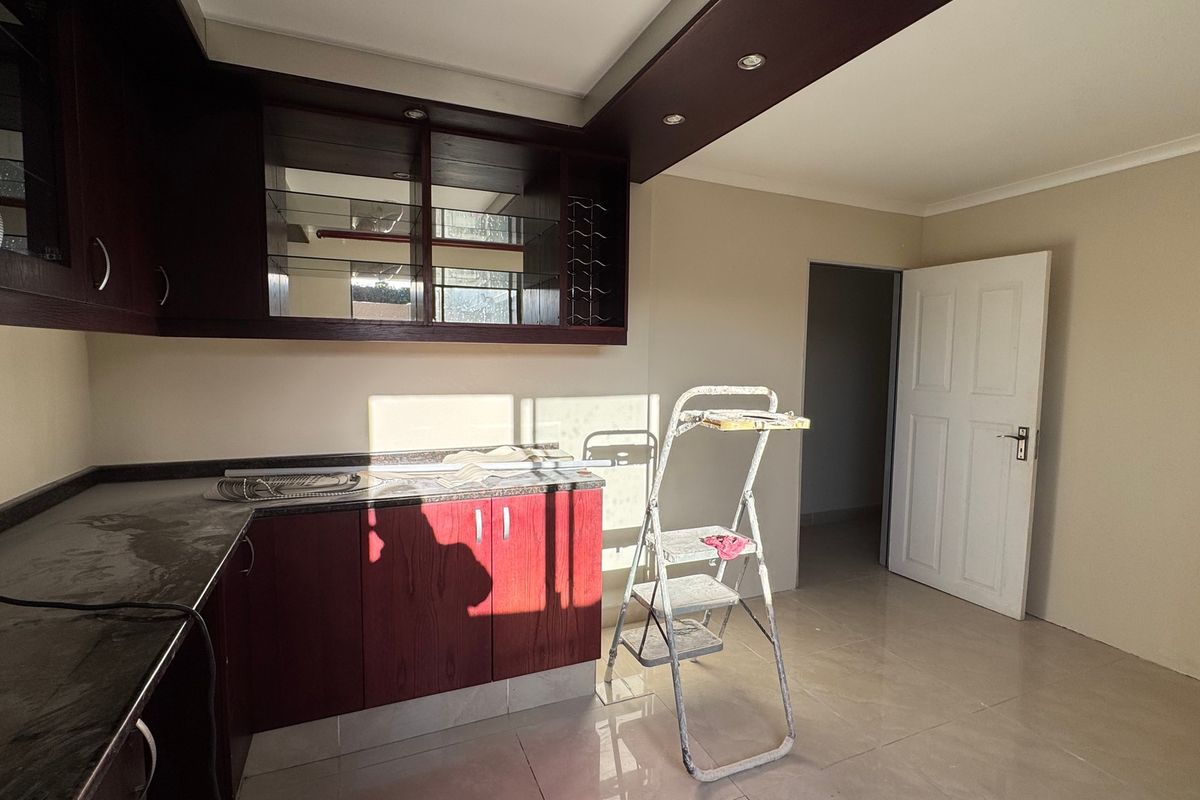 A functional kitchen area featuring dark wood-toned cabinetry, granite-look countertops, and neutral tiled flooring, currently in a vacant state.
