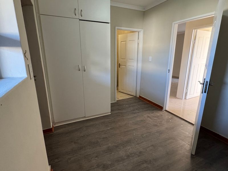 A clean, empty bedroom featuring built-in cupboards, modern laminate flooring, and neutral wall finishes, providing a versatile space ready for personalization.
