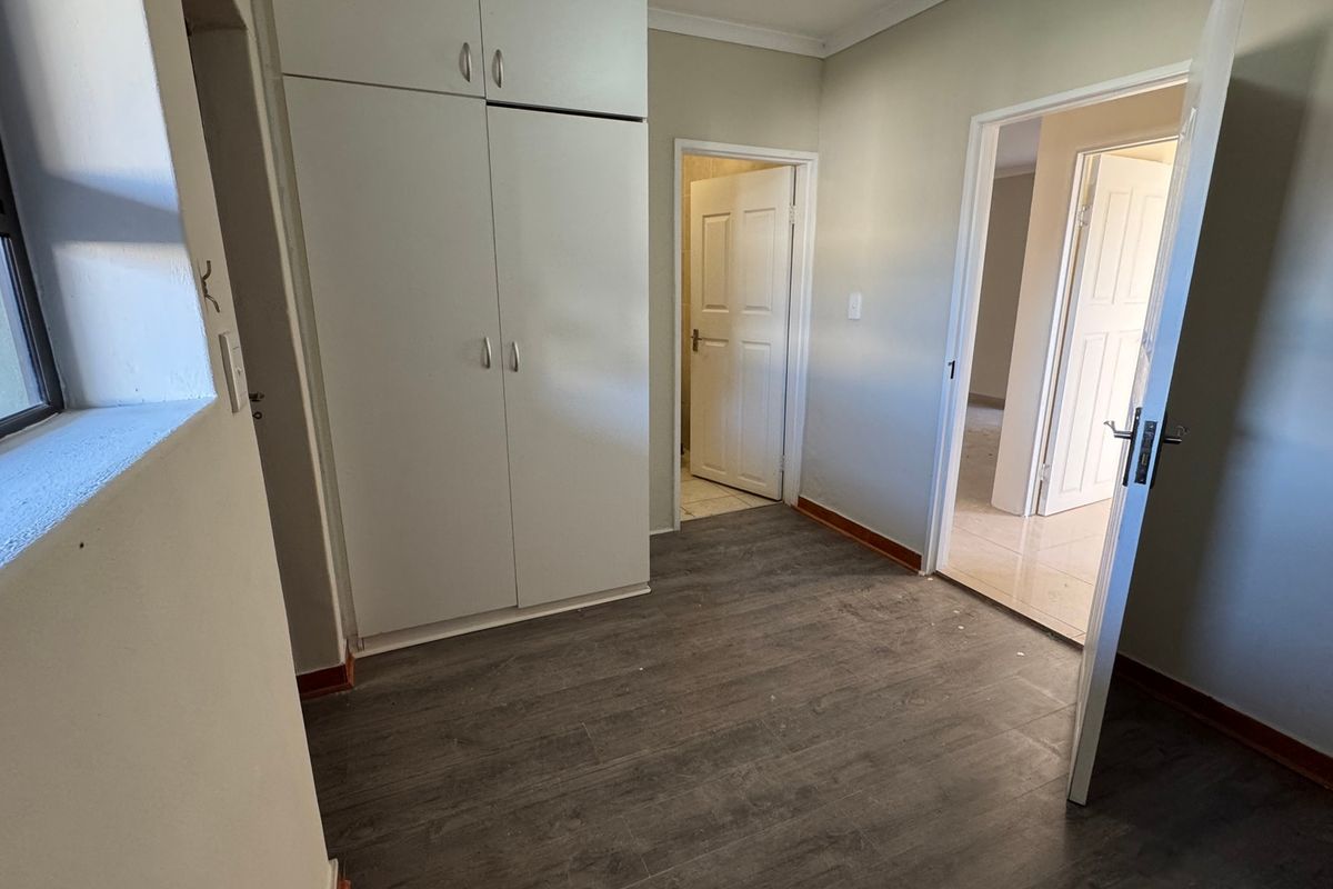A clean, empty bedroom featuring built-in cupboards, modern laminate flooring, and neutral wall finishes, providing a versatile space ready for personalization.