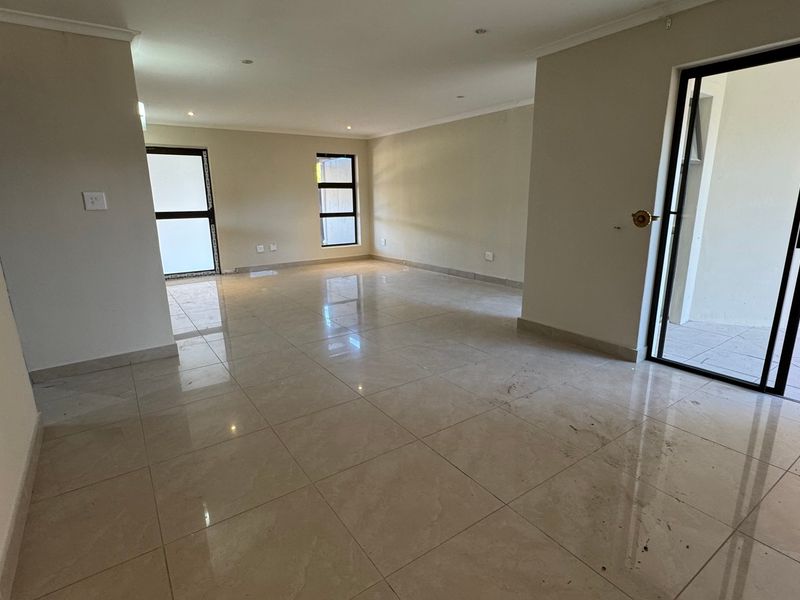 A spacious, empty living area featuring neutral tiled flooring, recessed lighting, and direct access to an outdoor patio through sliding glass doors.