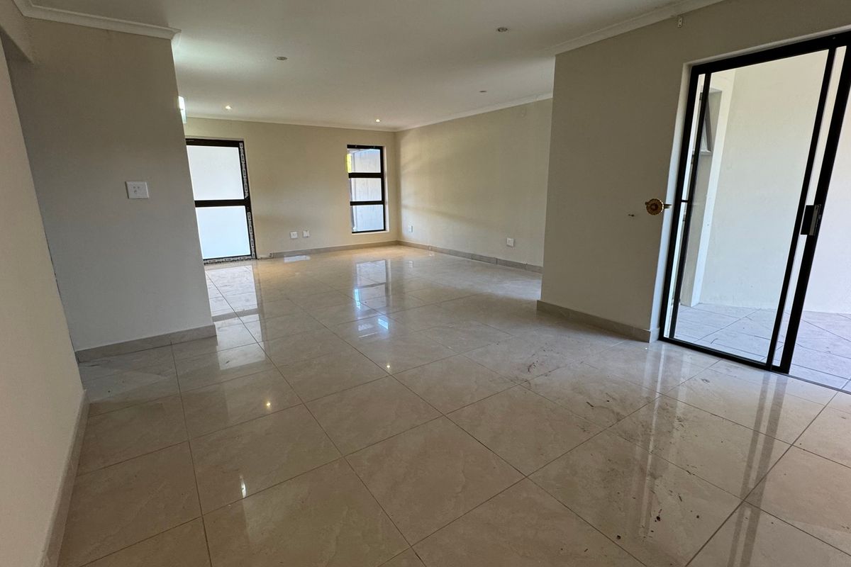 A spacious, empty living area featuring neutral tiled flooring, recessed lighting, and direct access to an outdoor patio through sliding glass doors.