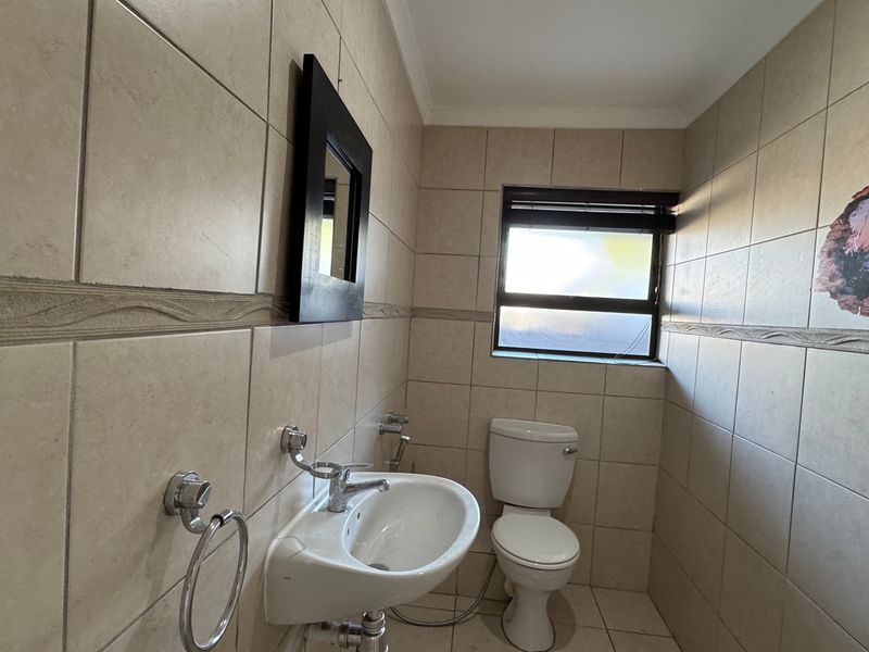 A functional bathroom featuring full-height ceramic wall tiling, a pedestal basin, and a standard toilet.