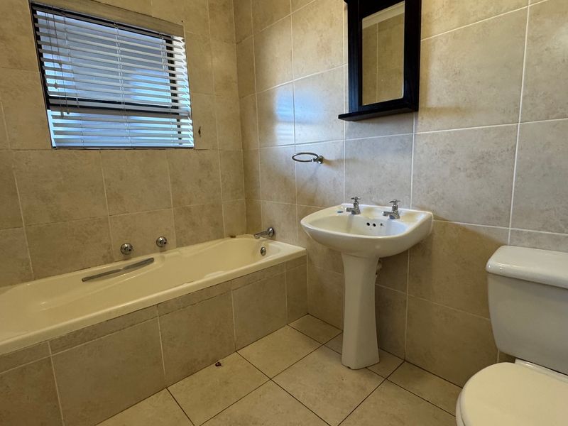A functional bathroom featuring a bathtub, pedestal sink, toilet, and neutral wall and floor tiling.