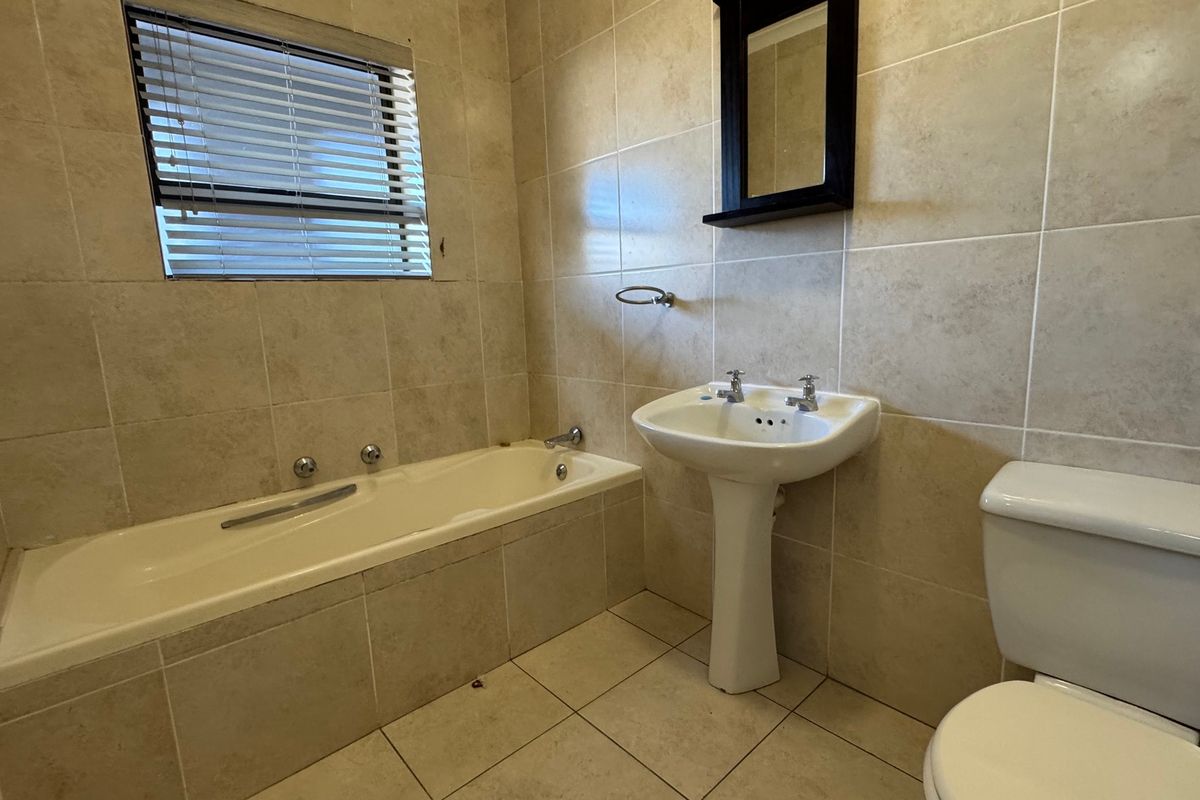 A functional bathroom featuring a bathtub, pedestal sink, toilet, and neutral wall and floor tiling.
