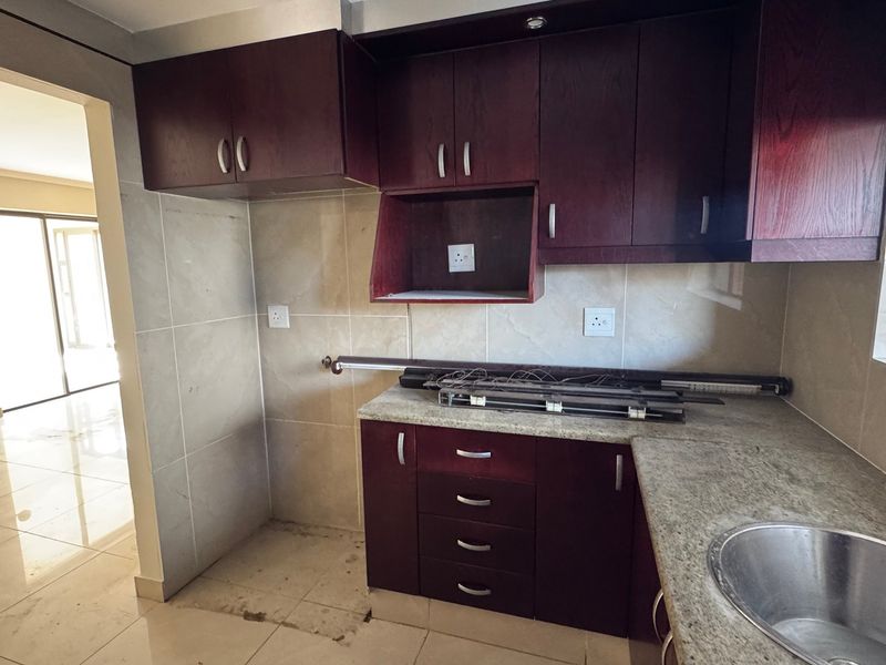 A functional kitchen featuring dark wood cabinetry, granite countertops, and a stainless steel sink, with an open-plan layout leading to the living area.