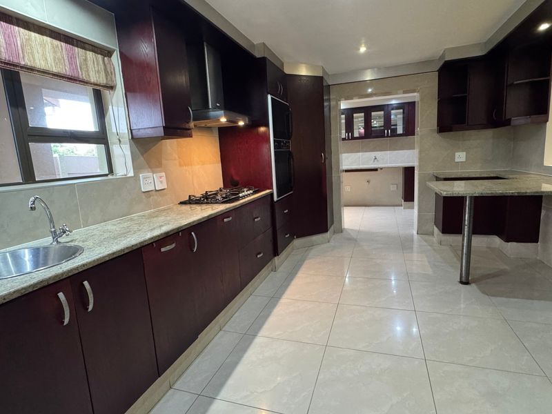 Spacious kitchen featuring dark wood cabinetry, granite countertops, built-in appliances, and a breakfast bar, leading into a separate scullery area.