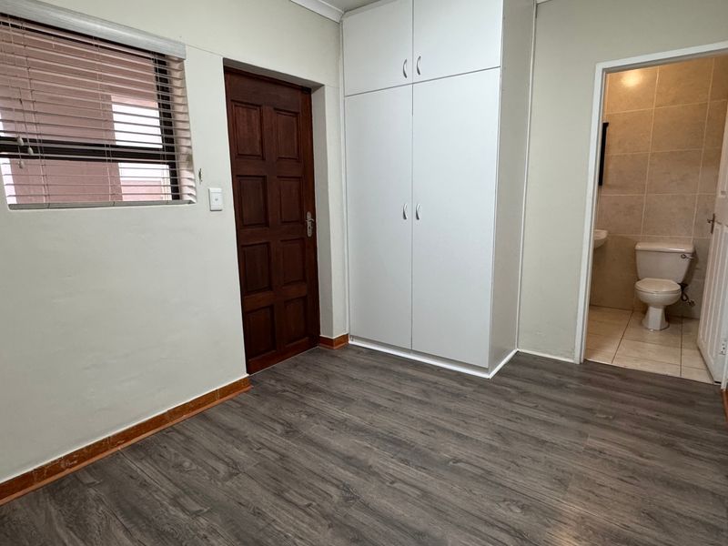 A clean, empty bedroom featuring laminate flooring, built-in cupboards, and an en-suite bathroom access.