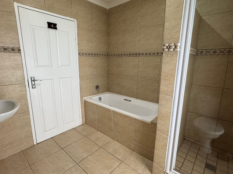 A functional bathroom featuring a built-in bathtub, separate shower enclosure, and wall-mounted basin with neutral ceramic tiling throughout.