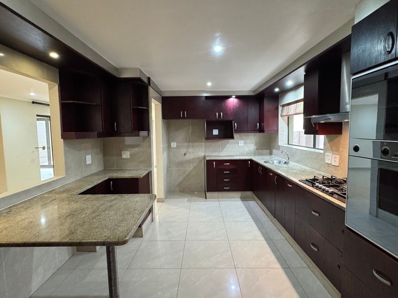 A spacious, modern kitchen featuring dark wood cabinetry, granite countertops, a built-in oven, gas hob, and tiled flooring.