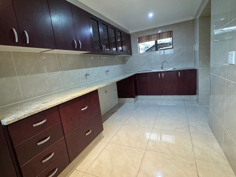 A clean and functional scullery featuring dark wood cabinetry, granite countertops, and full-height wall tiling with ample storage space.