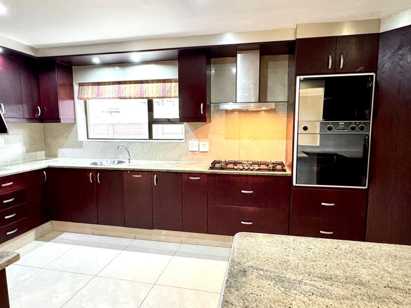 A well-appointed kitchen featuring dark wood cabinetry, granite countertops, a gas hob, extractor fan, and built-in oven with neutral tiled flooring.