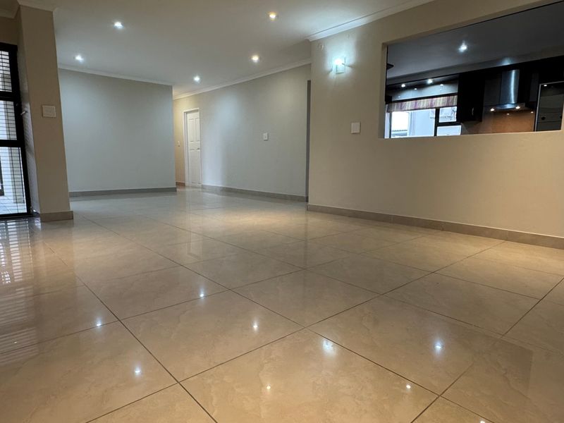 Spacious open-plan living area featuring neutral tiled flooring, recessed downlighting, and a convenient pass-through window connecting to the kitchen.