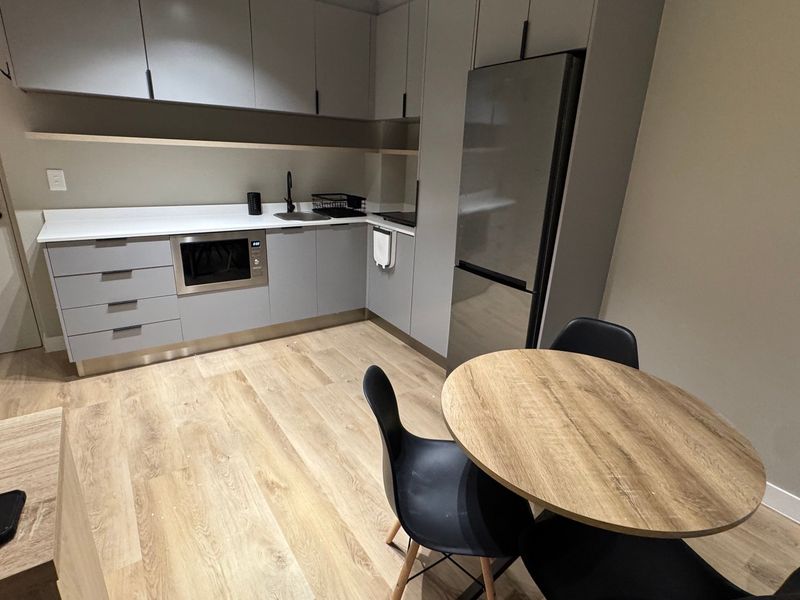 Modern kitchen featuring sleek grey cabinetry, stone benchtops, built-in microwave, and high-quality laminate flooring in a contemporary apartment setting.