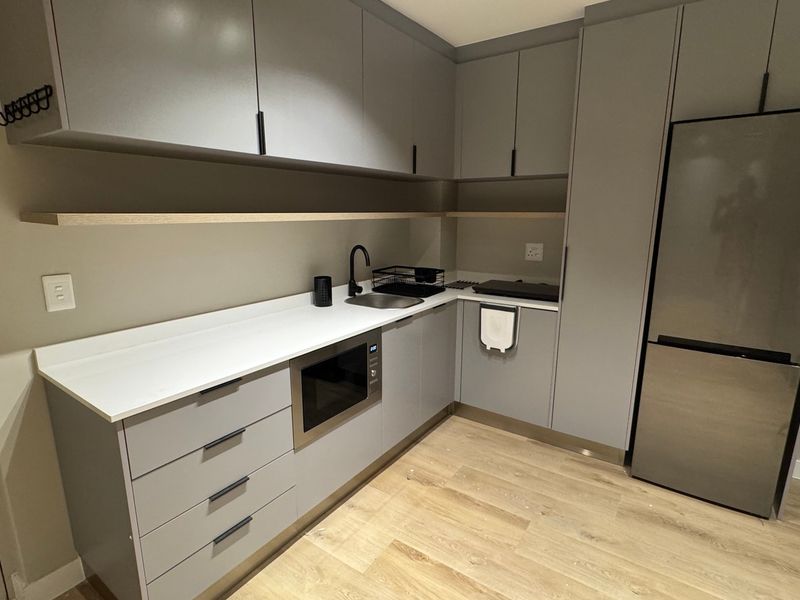 Modern kitchen featuring sleek grey cabinetry, stone countertops, integrated microwave, and high-quality laminate flooring in a clean, contemporary design.