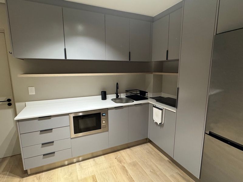 A modern, compact kitchen featuring sleek grey cabinetry, stone countertops, integrated appliances, and light wood-look flooring.