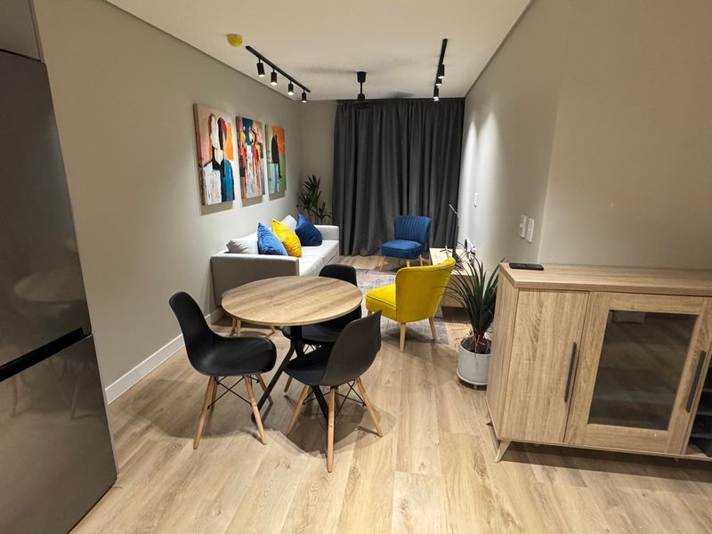A modern open-plan living and dining area featuring light wood-look laminate flooring, contemporary track lighting, and neutral wall finishes.