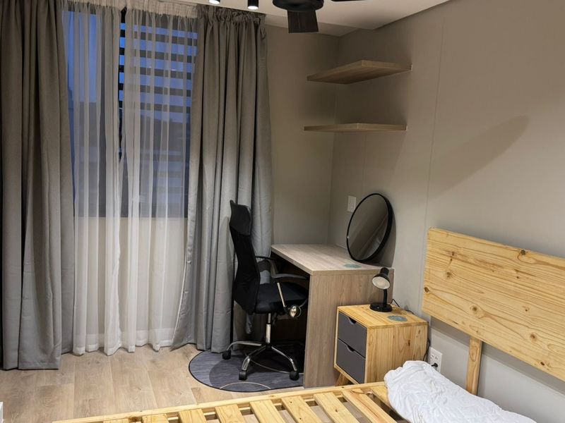 A well-maintained bedroom featuring neutral wall tones, laminate flooring, modern track lighting, and built-in wall shelving.