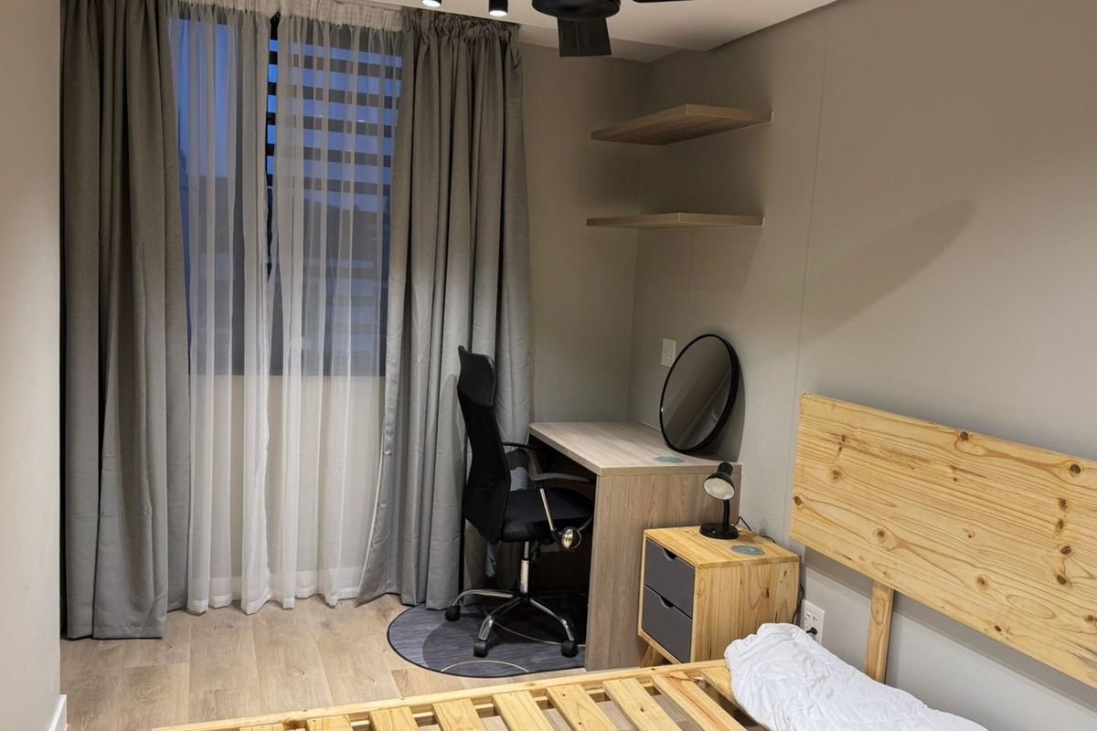A well-maintained bedroom featuring neutral wall tones, laminate flooring, modern track lighting, and built-in wall shelving.