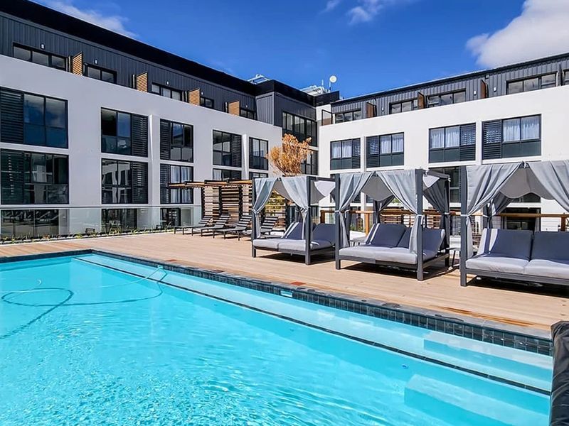 A well-maintained outdoor swimming pool area featuring timber decking and a modern multi-story apartment building facade.