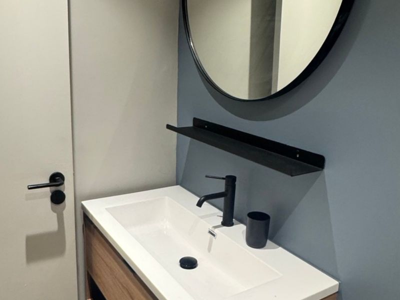 Modern bathroom vanity featuring a sleek integrated basin, matte black mixer tap, and a contemporary round mirror against a blue accent wall.