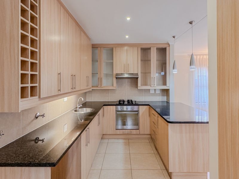 Modern kitchen featuring light wood cabinetry, granite countertops, built-in stainless steel appliances, and a functional U-shaped layout with tiled flooring.