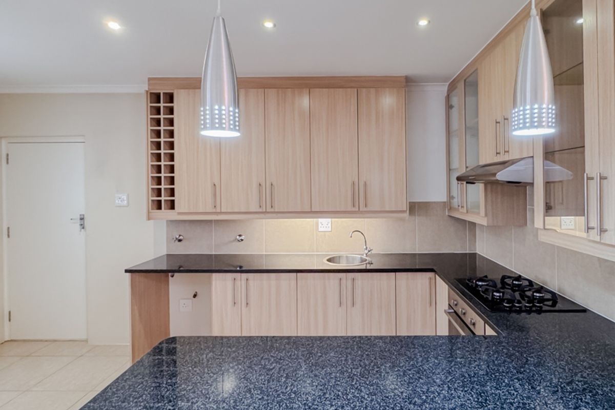 Modern kitchen featuring light wood cabinetry, dark granite countertops, integrated gas hob, extractor fan, and built-in oven with ample storage space.