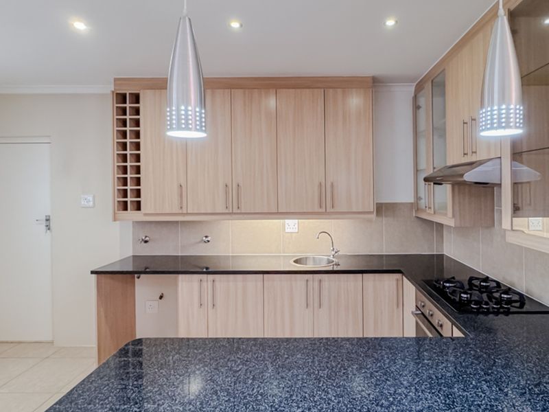 Modern kitchen featuring light wood cabinetry, dark granite countertops, integrated gas hob, extractor fan, and built-in oven with ample storage space.