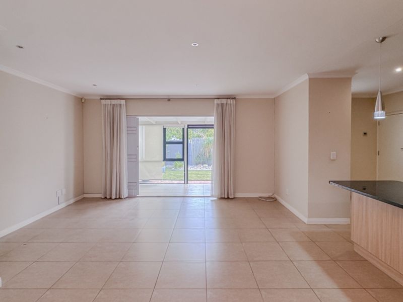 Spacious open-plan living area featuring tiled floors, recessed lighting, and a modern kitchen with granite countertops, flowing seamlessly to an outdoor patio.
