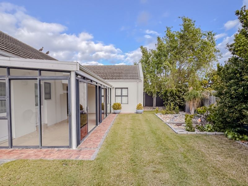 A well-maintained rear exterior view featuring a paved patio area, sliding glass doors, and a landscaped garden with a rock feature.