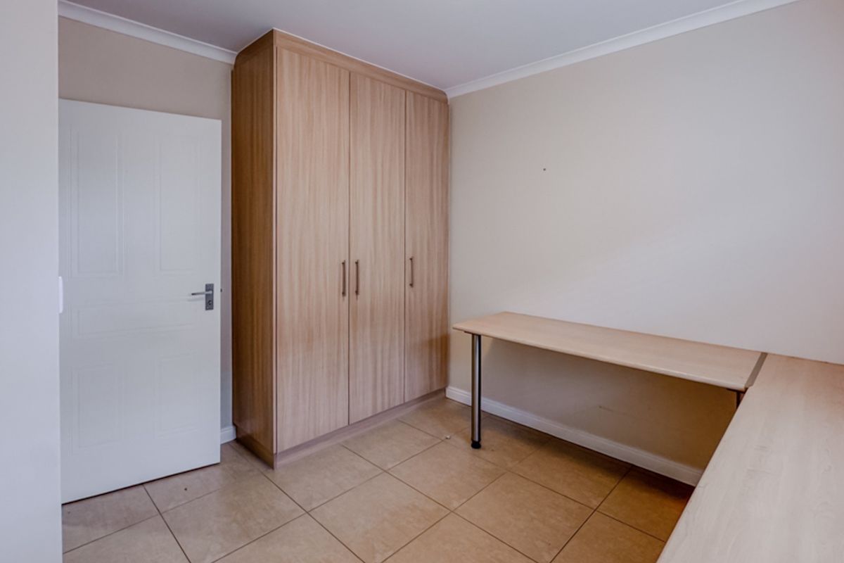 A clean, neutral bedroom featuring built-in wooden cabinetry, a fitted desk, and tiled flooring, offering a versatile space for a bedroom or home office.