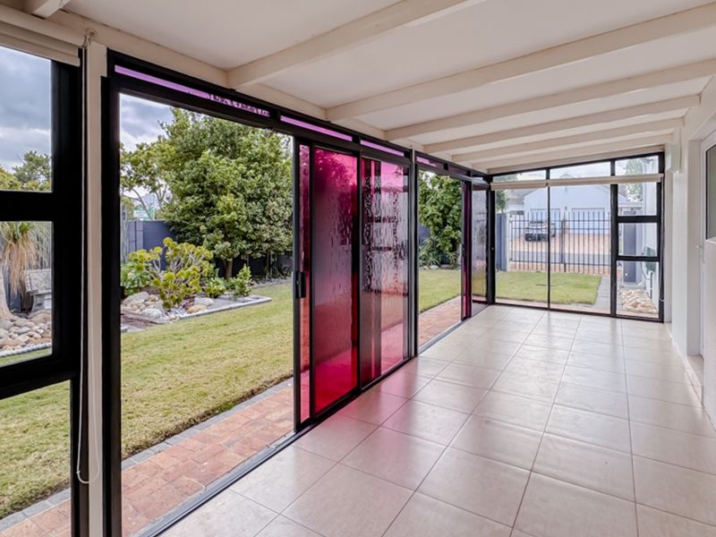 A bright, enclosed patio area featuring tiled flooring, exposed beam ceilings, and large sliding glass doors that open onto the garden.
