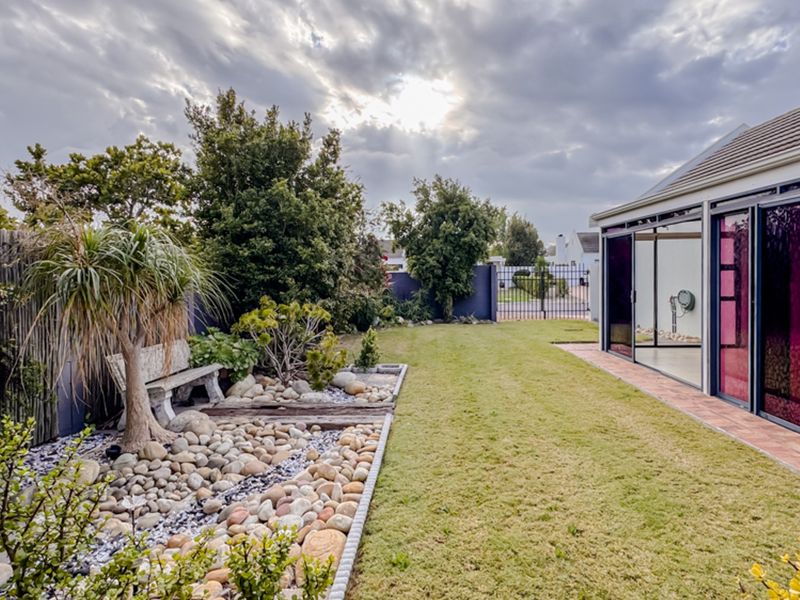 A well-maintained rear garden featuring a landscaped pebble bed, lawn area, and a tiled patio accessible through large sliding glass doors.