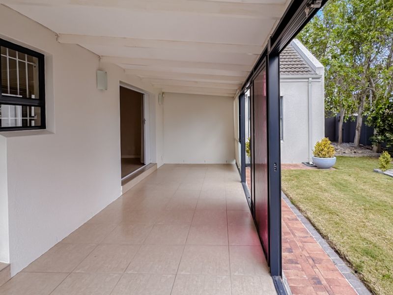 A spacious covered patio featuring tiled flooring and sliding glass doors, providing seamless access to the rear garden and lawn area.