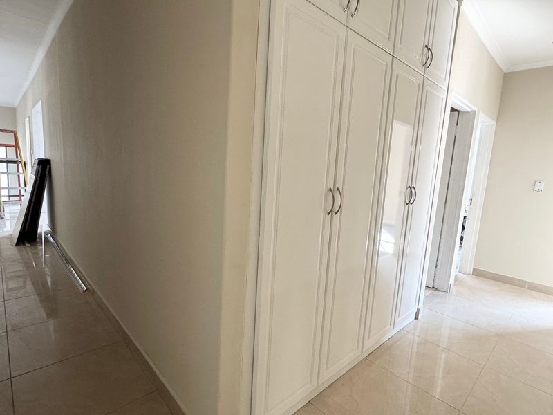 A bright, spacious hallway featuring neutral tiled flooring, recessed lighting, and extensive built-in cabinetry for storage.