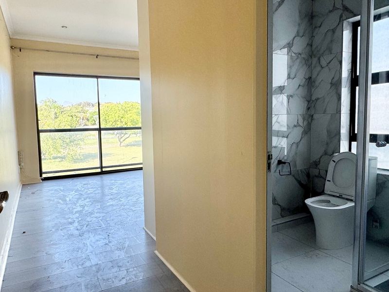 An empty bedroom featuring a large sliding glass door with garden views and an adjacent en-suite bathroom with marble-look wall tiles.