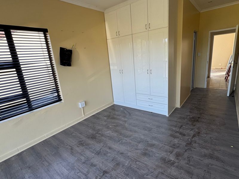 A vacant bedroom featuring built-in white cupboards, dark laminate flooring, and venetian blinds on the window.