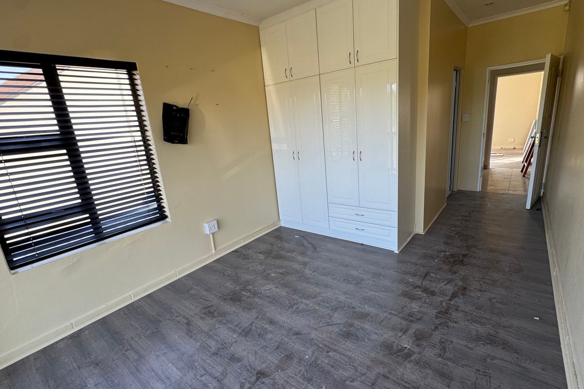 A vacant bedroom featuring built-in white cupboards, dark laminate flooring, and venetian blinds on the window.