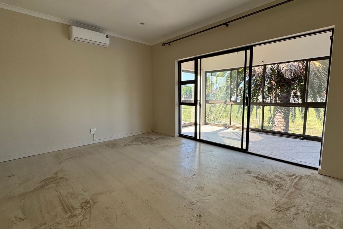 An empty living room featuring tiled flooring, a wall-mounted air conditioner, and large sliding glass doors providing access to an outdoor patio area.