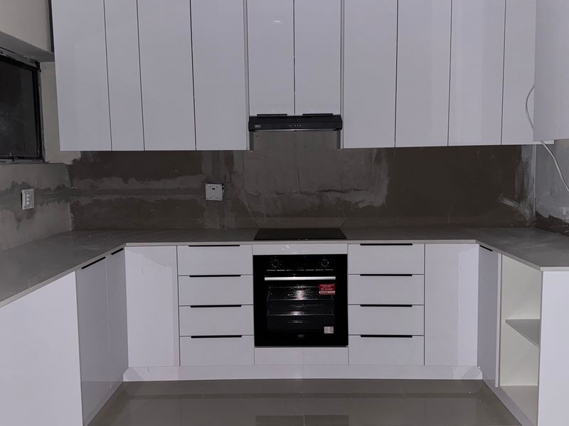 A modern kitchen featuring white cabinetry and built-in appliances, currently requiring backsplash installation and final electrical finishing to complete the space.