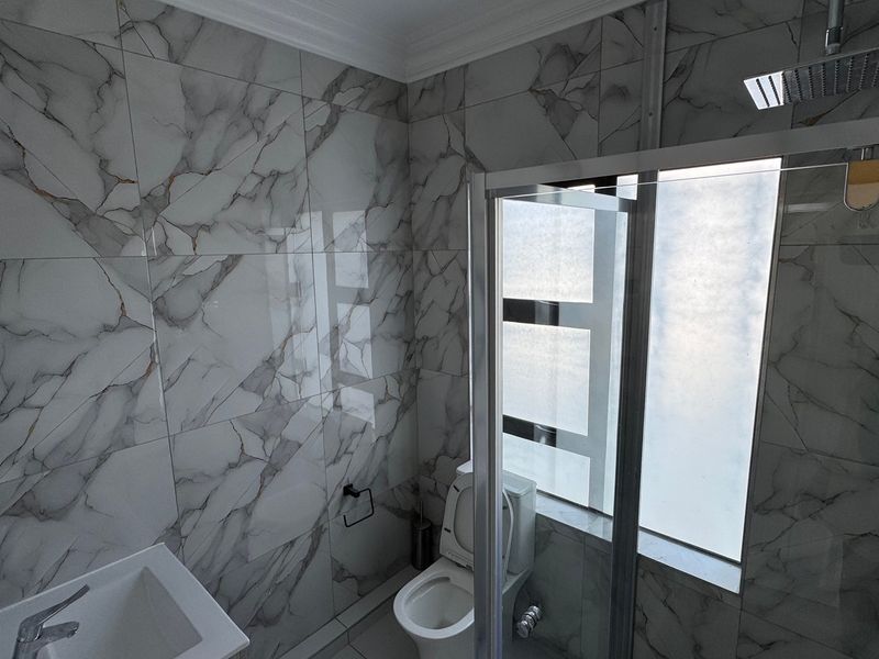 Modern bathroom featuring floor-to-ceiling marble-look wall tiles, a walk-in shower with a rain shower head, and a contemporary basin and toilet.