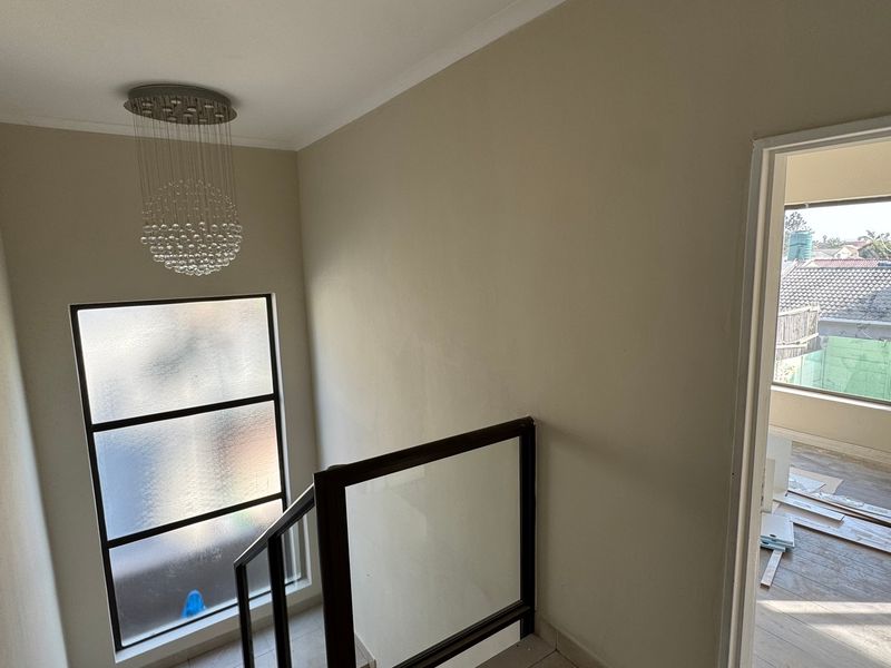 A bright hallway featuring a modern glass balustrade, a contemporary pendant light, and a large frosted window providing natural light.