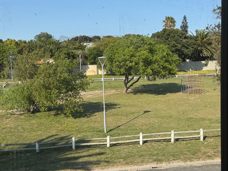 A pleasant view overlooking a well-maintained communal green space with mature trees, fencing, and street lighting.