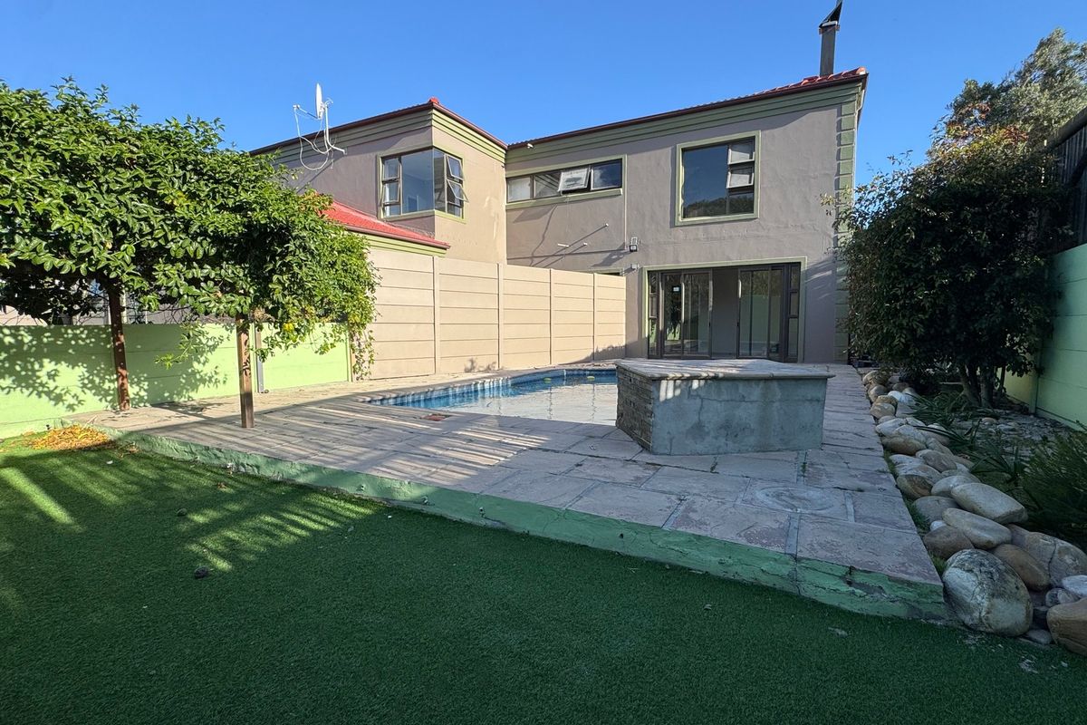 Rear exterior view featuring a swimming pool, paved patio area, and artificial lawn, enclosed by a boundary wall with direct access to the house.