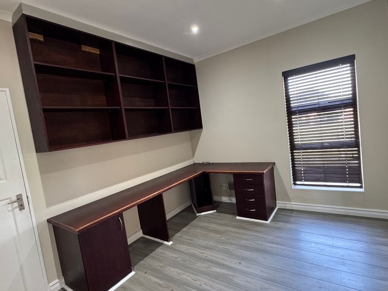 A dedicated home office featuring built-in dark wood cabinetry, a spacious desk area, laminate flooring, and window blinds.