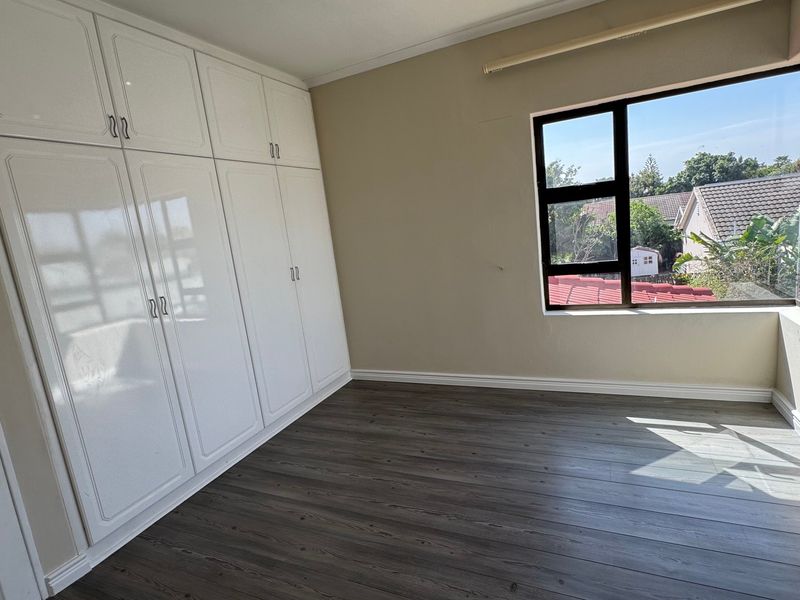 A bright, empty bedroom featuring modern laminate flooring, neutral walls, and extensive white built-in cupboards with ample storage space.