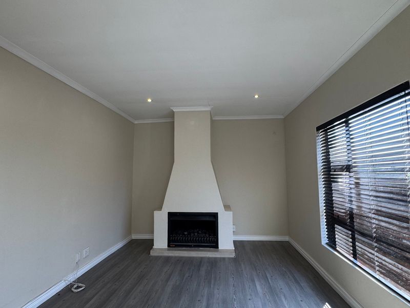 A bright, empty living room featuring modern laminate flooring, a central built-in fireplace, and venetian blinds on the window.